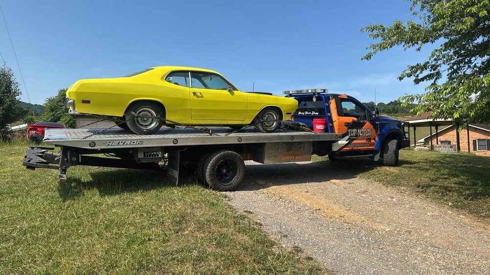 A yellow classic Plymouth Duster chained down on the Top Notch blue and orange flatbed wrecker