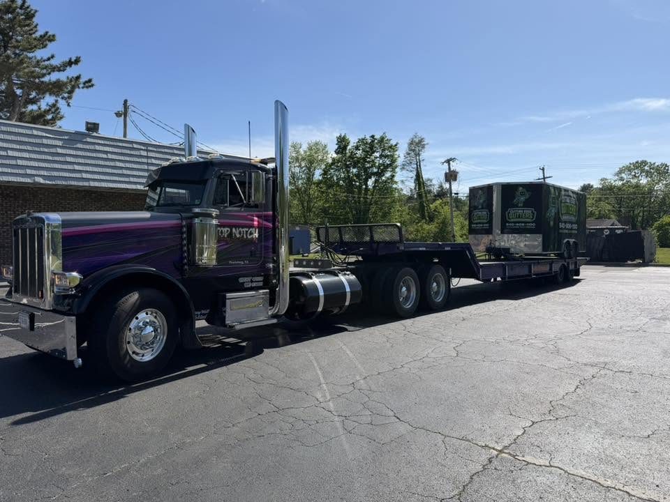 The Top Notch Peterbilt with a drop-deck trailer moving an enclosed equipment trailer